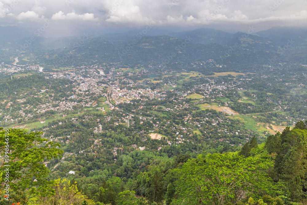 Obraz premium View from Ambuluwawa Tower, multi-religious temple complex located in Gampola, in Sri Lanka. Panoramic Aerial View of a Vibrant Town Nestled Amidst Lush Green Hills and Clouds