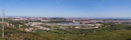 Alcabideche, Portugal - 03 April 2026: Aerial view of Autodromo Fernanda Pires da Silva racing circuit with its winding track, grandstands, and surrounding green hills under a clear blue sky.