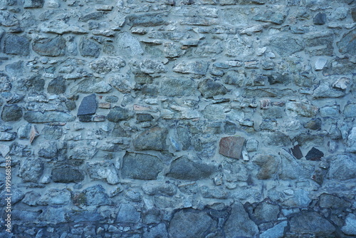 Rugged Grey Stone Wall Texture with Irregular Rock Pattern and Cold Blue Tone, Ancient Medieval Rubble Masonry Background, Historic Fortress Architecture Surface, Organic Hard Rock Detail.