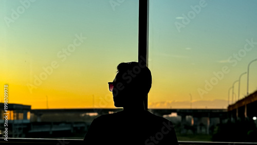 Silhouette of person looking at sunset through window with warm light tones
