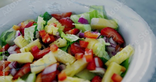 Showing white bowl with lettuce, pineapple, strawberries, cucumber, red onion, pepper on gray table