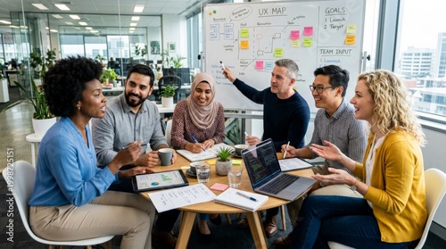 Diverse product development team collaborating on UX map whiteboard in modern office with laptops and tablets. User experience design, agile methodology, cross-functional teamwork.