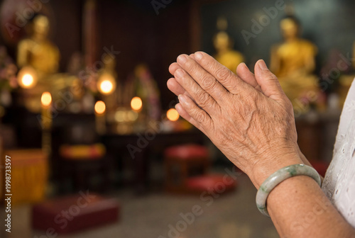 Elderly asian woman with hands clasped in prayer at a buddhist temple