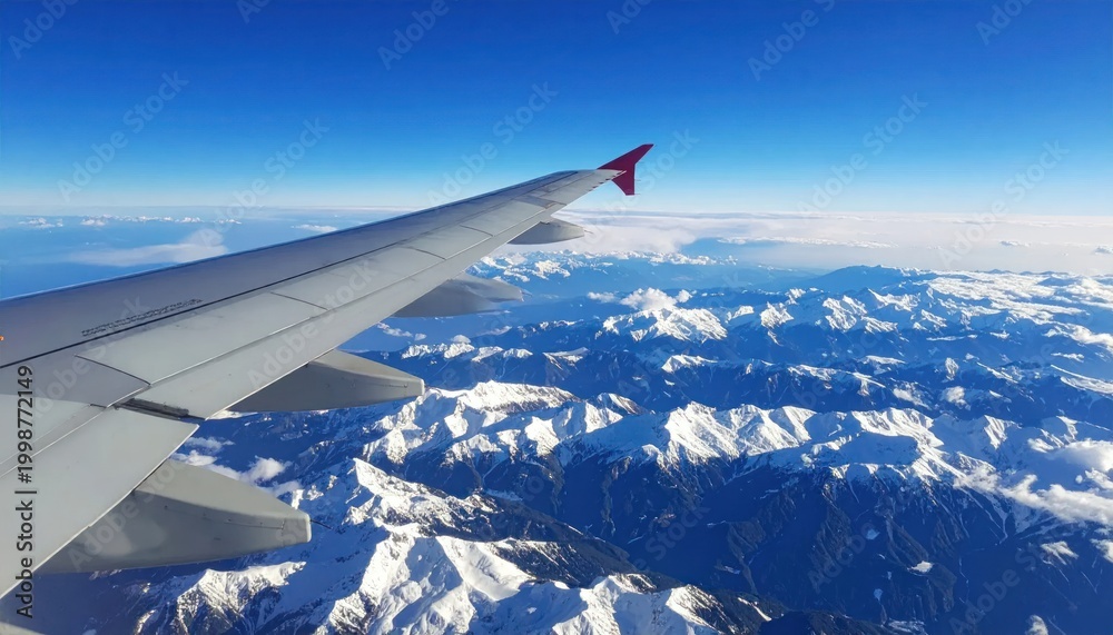 Fototapeta premium Airplane Wing Over Snowy Mountain Range Under Blue Sky.