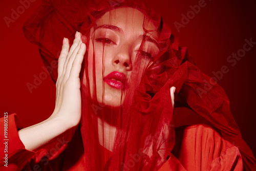 Fotografía Fashion portrait of young woman with bright red tulle veil over face wearing red robe