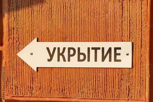 White arrow sign with Shelter inscription in Cyrillic pointing left on textured orange facade in Russia