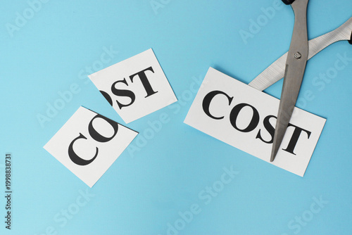 Фотография Scissors cutting the word COST on a blue background, representing cost reduction, budgeting efficiency, financial control, and smart savings strategies in modern business management