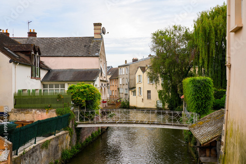 Charming view of the Blaise river in Dreux, France, featuring a white decorative footbridge and traditional houses with gardens