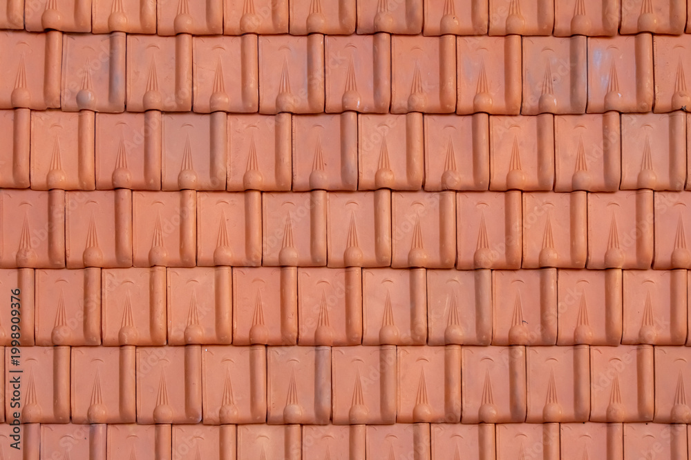 Fototapeta premium close-up photograph displays a uniform pattern of burnt orange, terracotta-style roof tiles. The tiles are interlocking, with rounded upper parts and decorative lines.