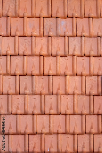 close-up photograph displays a uniform pattern of burnt orange, terracotta-style roof tiles. The tiles are interlocking, with rounded upper parts and decorative lines.