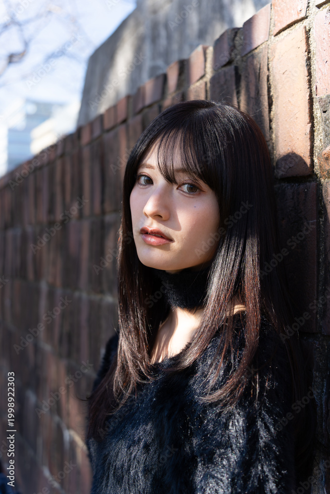 Fototapeta premium 木漏れ日が顔に差す、冬の装いの女性。屋外でのファッションポートレート