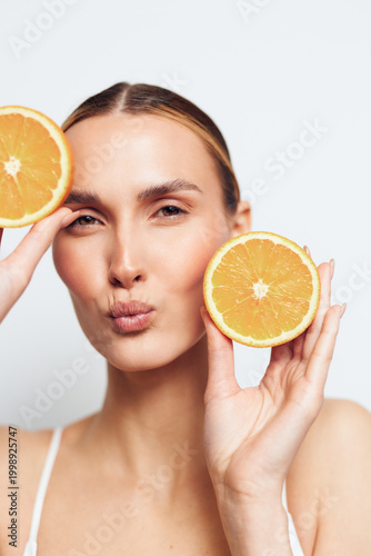 Woman holds orange citrus slices by cheeks for natural skincare beauty, fresh healthy spa concept, vitamin c hydration and glow on isolated portrait, studio light on white background