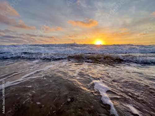 Foto Three distinct waves breaking in succession during a vibrant sunset at Carlsbad State Beach