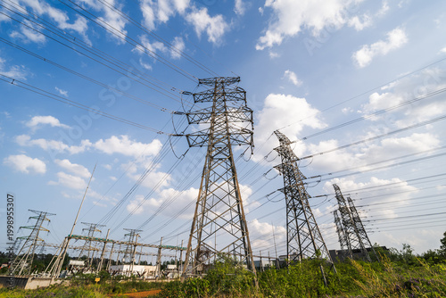 Foto Multiple steel lattice transmission towers and power lines stand in a grassy field under a blue cloudy sky, part of electrical power infrastructure
