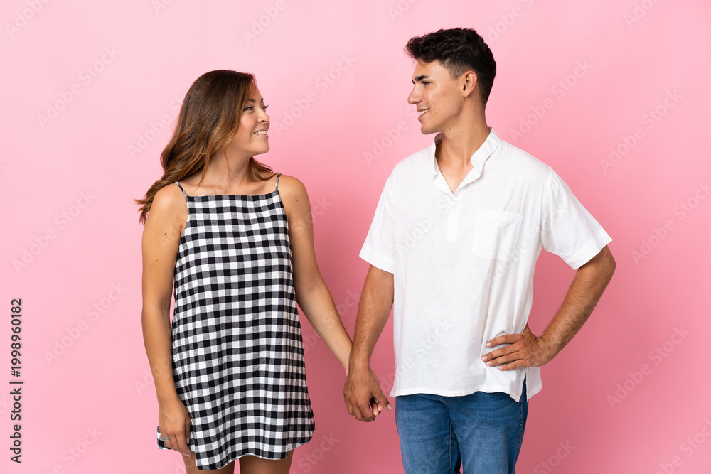 Fototapeta premium Young caucasian couple isolated on pink background looking at each other