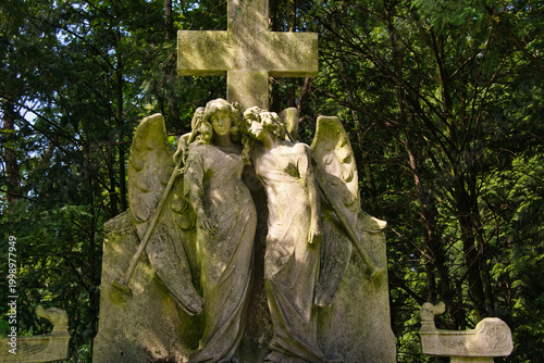zwei große schöne Engel vor einem Steinkreuz auf einem Friedhof in Köln