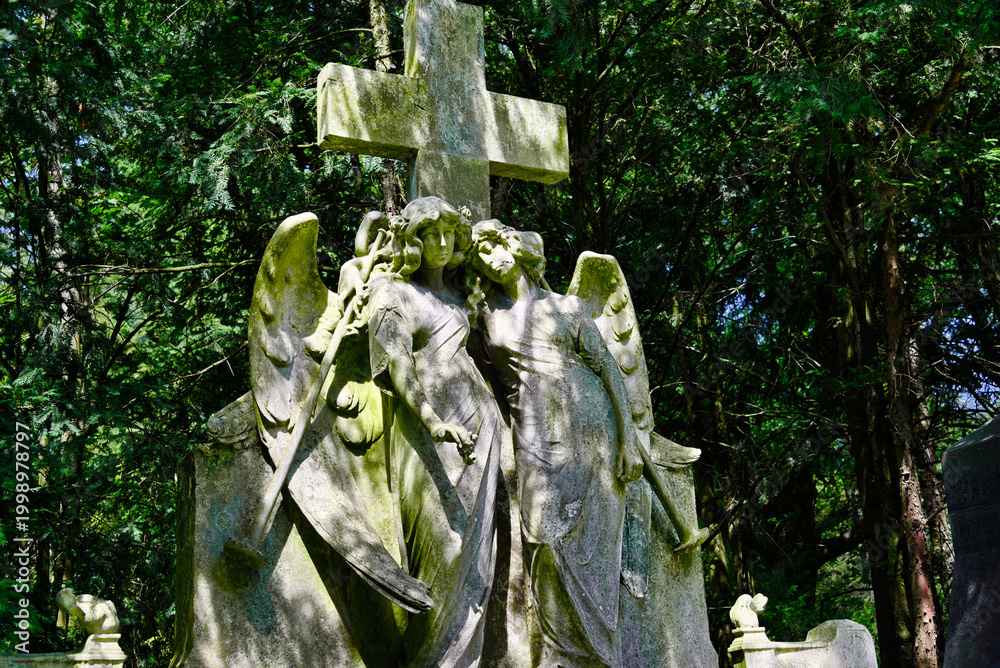 Fototapeta premium zwei Engel unter einem Steinkreuz auf einem Friedhof in Köln 