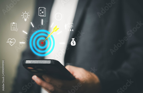 Person using smartphone with digital target and business strategy icons, representing goal setting, KPI tracking, performance management, strategic planning, and business success.