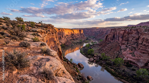 Cliff with rocky outcroppings and sparse vegetation overlooks expansive canyon and rugged landscape below