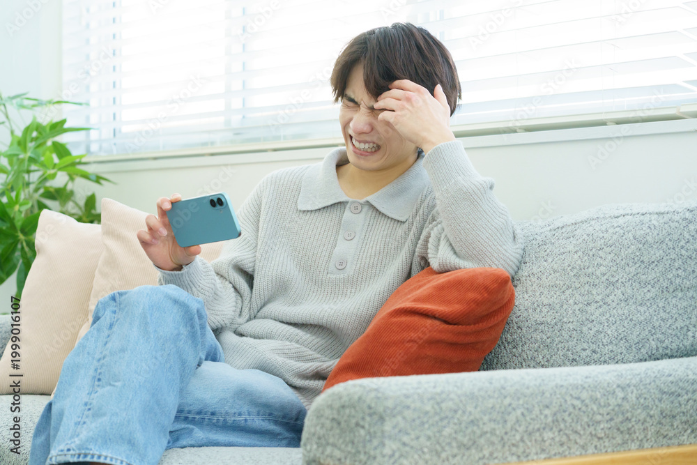 Obraz premium リビングでスマホで動画を視聴する落ち込む日本人男性
