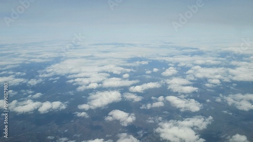 Photography Aerial view above clouds with scattered formations over land, showing a serene sky scene with soft light and endless horizon, evoking a sense of freedom and peaceful travel