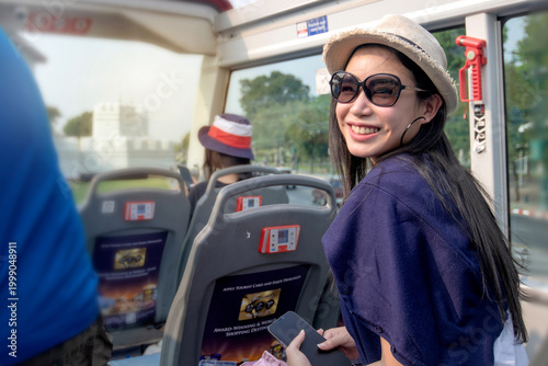 An Asian female tourist enjoyed a tour by open-top bus.