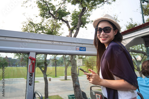 An Asian female tourist enjoyed a tour by open-top bus.