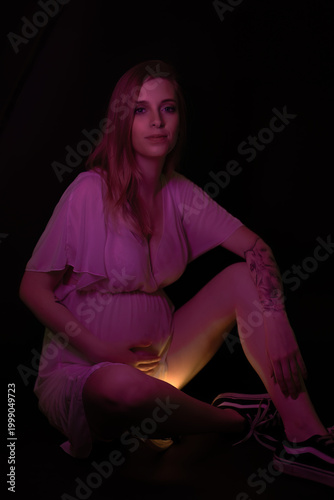 Young pregnant woman illuminated by pink fluorescent light