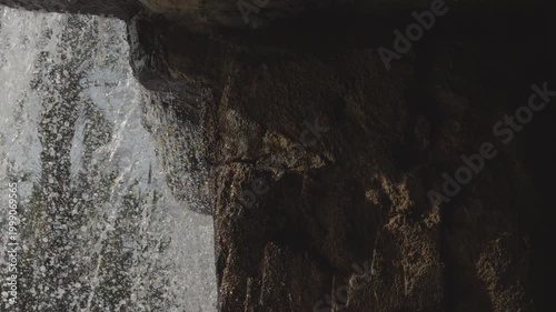 Water splashing and flowing over dark natural rock surface in close up