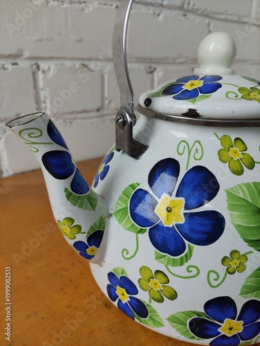 Enamel painted kettle with flowers on table against white brick wall