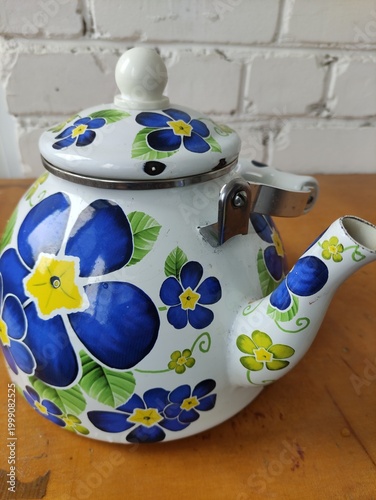 Enamel painted kettle with flowers on table against white brick wall