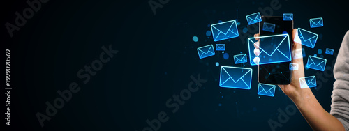 Digital email icons floating around a smartphone held by a person on dark bac...