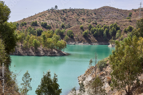 Turquoise lake reflecting surrounding green hills and sparse forest