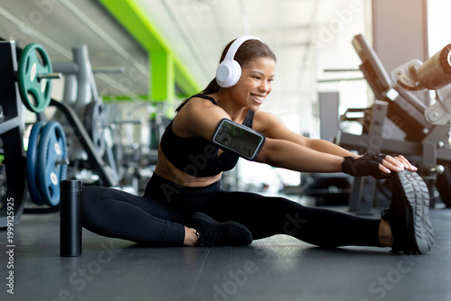 фотографія Happy young Black woman doing seated side split stretch on gym floor, smiling, w
