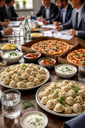 Business professionals enjoying catered lunch meeting with pizza, dumplings, and various dishes on conference table. Corporate catering spread with multiple food options.