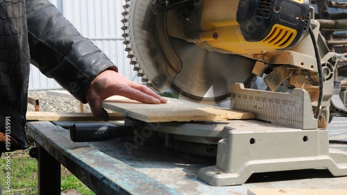 A close-up of a workman working on a miter saw during the process of cutting a board, the hands of a carpenter on the lever of a circular saw, cutting the end of a board