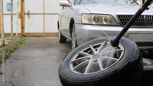 Washing car tires with a hose and a watering can in the yard of a house against the background of a gray car, tire care when changing a tire