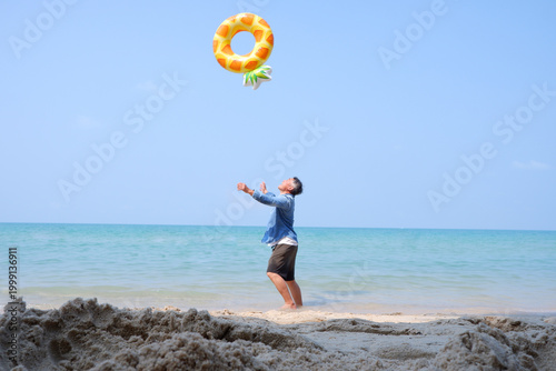 An elderly man joyfully tosses a swim ring by the calm seaside.