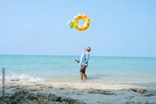 An elderly man joyfully tosses a swim ring by the calm seaside.