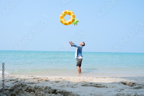 An elderly man joyfully tosses a swim ring by the calm seaside.
