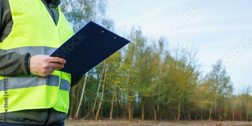Photography Close-up view of hands inspector holding a clipboard against a woodland background in early spring
