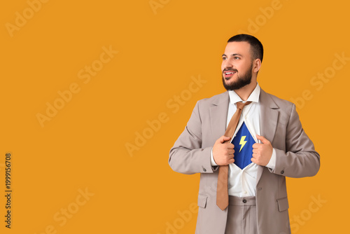 Young businessman in superhero costume under his suit on orange background