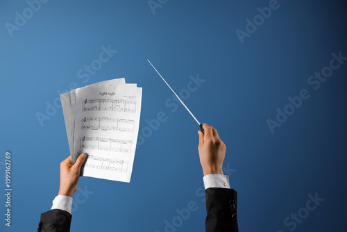 Tablou pe pânză Male conductor's hands with note sheets on blue background