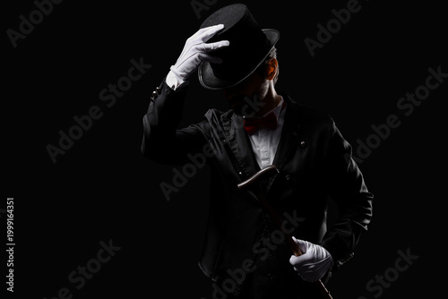 Vászonkép Male magician with hat and stick on black background