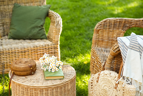 Schilderij op canvas Comfortable wicker armchairs with chamomile flowers, book and bags on coffee tab