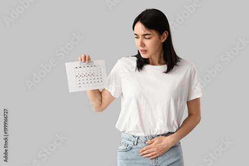 Young woman with calendar suffering from menstrual cramps on light background