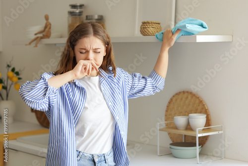 Young woman suffering from dust allergy while cleaning kitchen