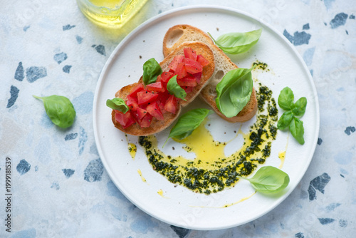 White plate with tomato bruschettas and basil oil, horizontal shot on a white and blue granite background, elevated view