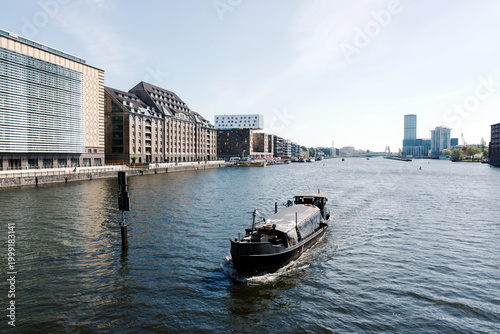Freight barge sailing on Berlin Spree River with waterfront buildings and skyscraper
