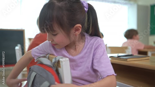 Students turn to retrieve their stationery from backpacks hanging behind their chairs, while students and teachers of diverse nationalities are engaged in activities